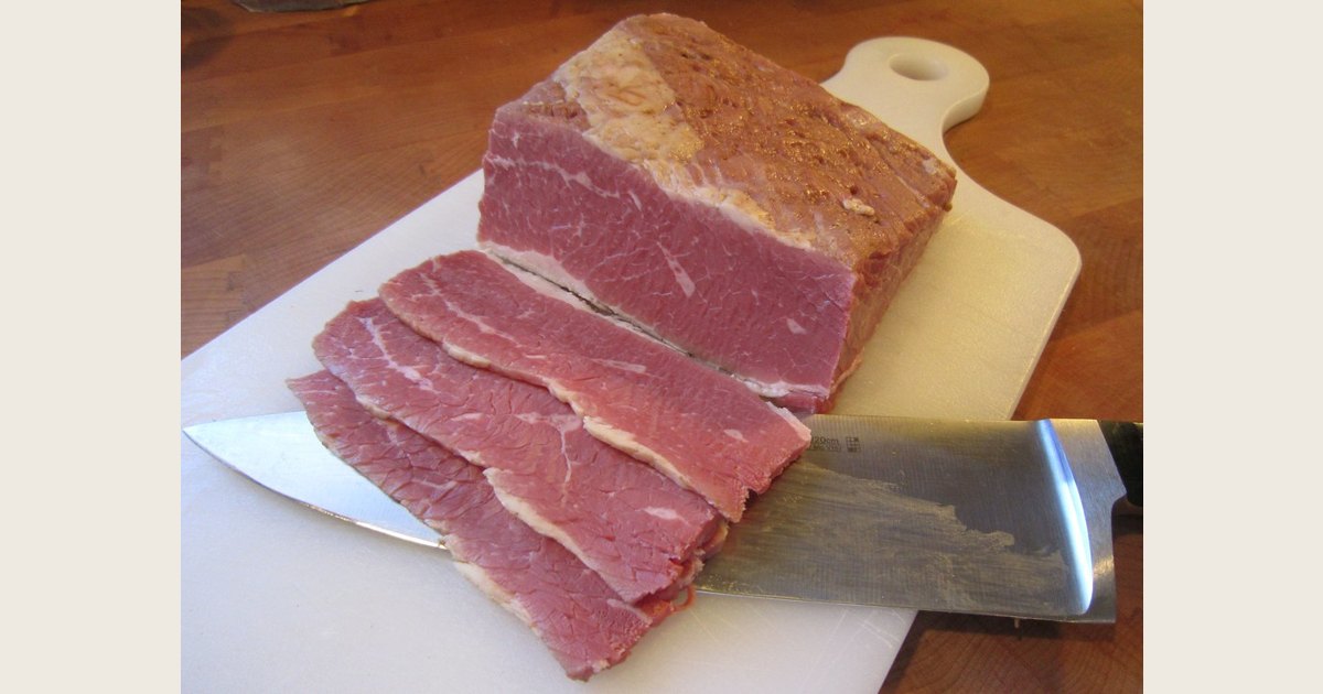 Corned beef on a cutting board with thin slices beside the remaining piece