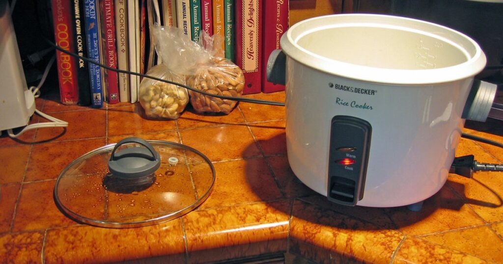 A white countertop electric rice cooker with a rounded lid and front control panel.