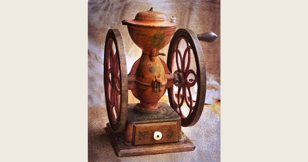 Antique hand-cranked coffee grinder with a covered hopper