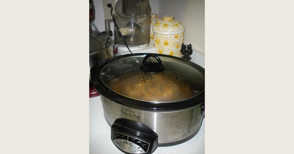 An open slow cooker holding browned pieces of meat in cooking liquid.