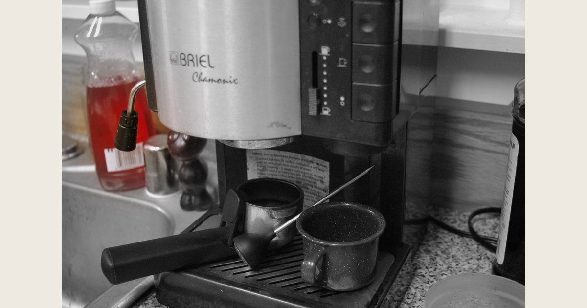 A countertop espresso machine with a portafilter and cups arranged on its drip tray.
